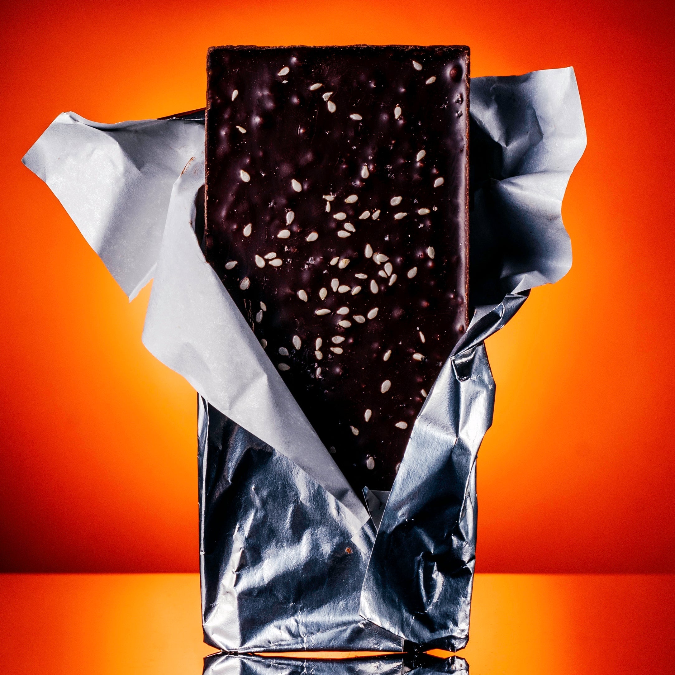 Dark chocolate bar with seeds wrapped in silver foil against an orange background